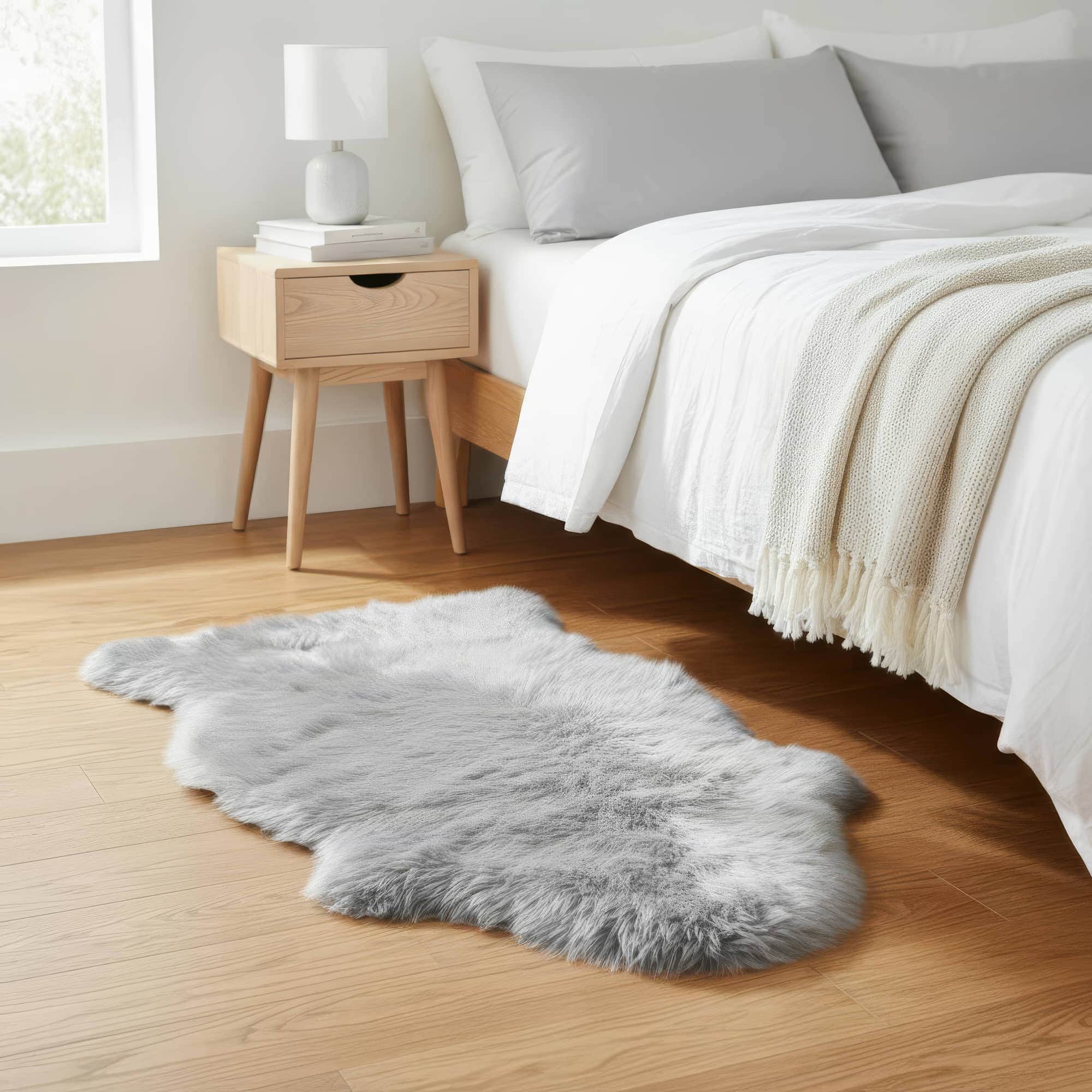 Gray fur rug on a wooden floor in a bedroom with a bed and nightstand. #size_2' x 3'