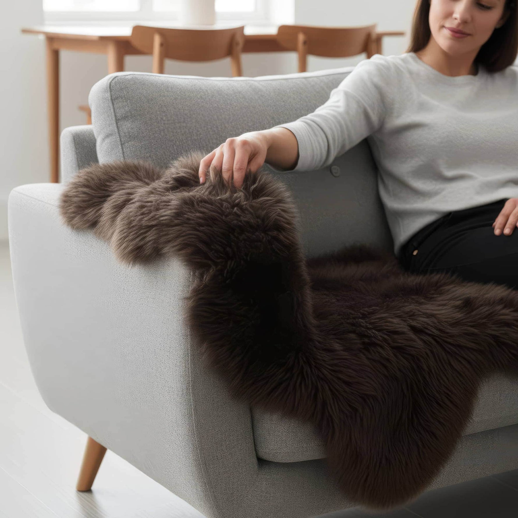 Woman sitting on a gray sofa with a brown fur throw draped over it in a bright room. #size_2' x 3'